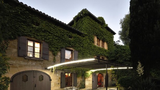 A stone building with ivy-covered walls, a covered patio with chairs, and a large wooden door. - Le Moulinois - GLEIZE (GLEIZE)