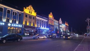 Una calle flanqueada por edificios con iluminación brillante, incluyendo un hotel con señalización en idioma extranjero.