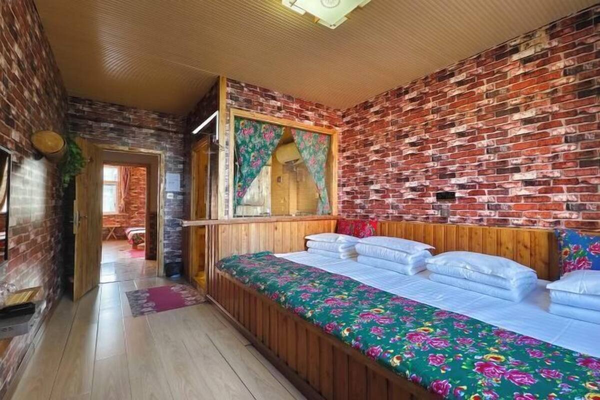 A room with a brick wall, wooden bed, and a window with curtains.