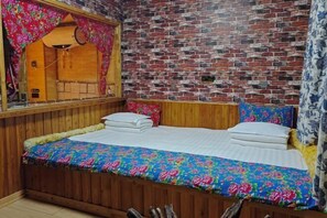 Una habitación con pared de ladrillo, estructura de cama de madera, colcha estampada con motivos florales y espejo con cortina floral.
