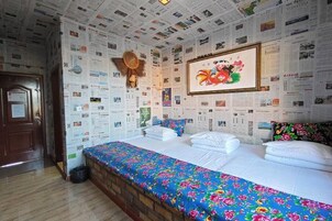 Una habitación con una cama cubierta de sábanas blancas, un edredón floral de colores y una pared decorada con numerosas fotos pequeñas.