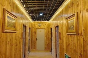 Un pasillo de madera con cuadros en las paredes, una puerta al final y un cartel a la derecha.
