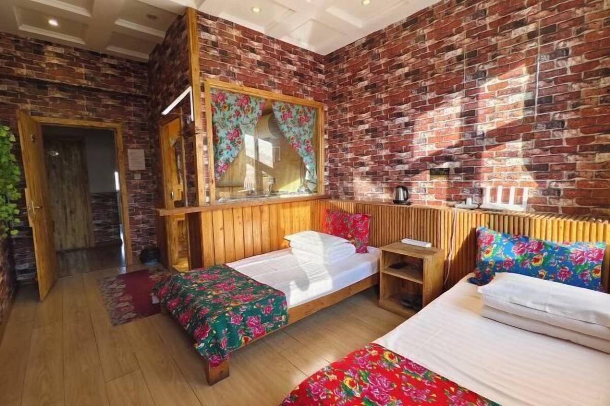 A room with a brick wall, wooden bed frames, and a large window with floral curtains.