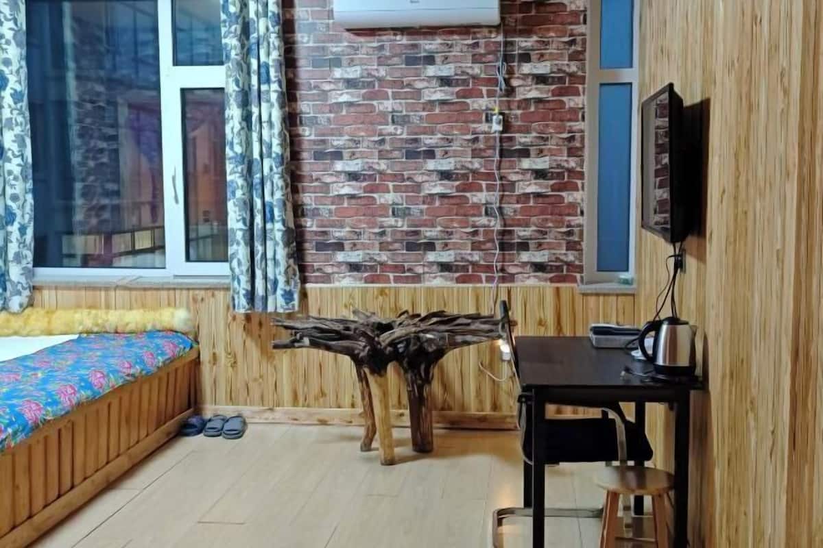 A room with a bed, a wooden table, a TV, and a brick wall.