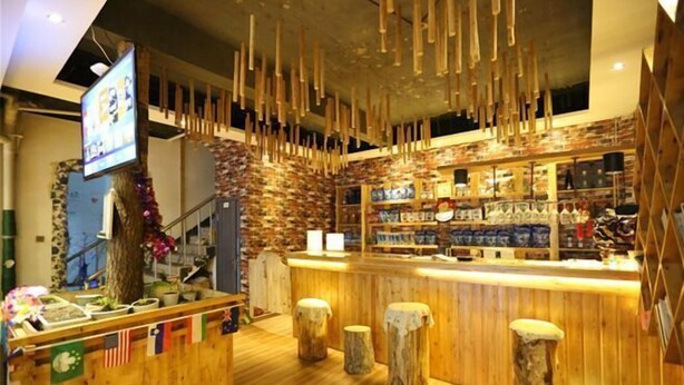 Una zona de bar con barra de madera, taburetes, una pantalla de televisión y estantes con productos.
