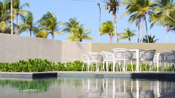 Una piscina con sillas blancas y palmeras al fondo.