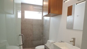 A modern bathroom with a glass shower enclosure, a white toilet, a white sink with a rectangular basin, and a mirror above the sink. - Hotel Miragua Playa El Agua (Paraguachí)