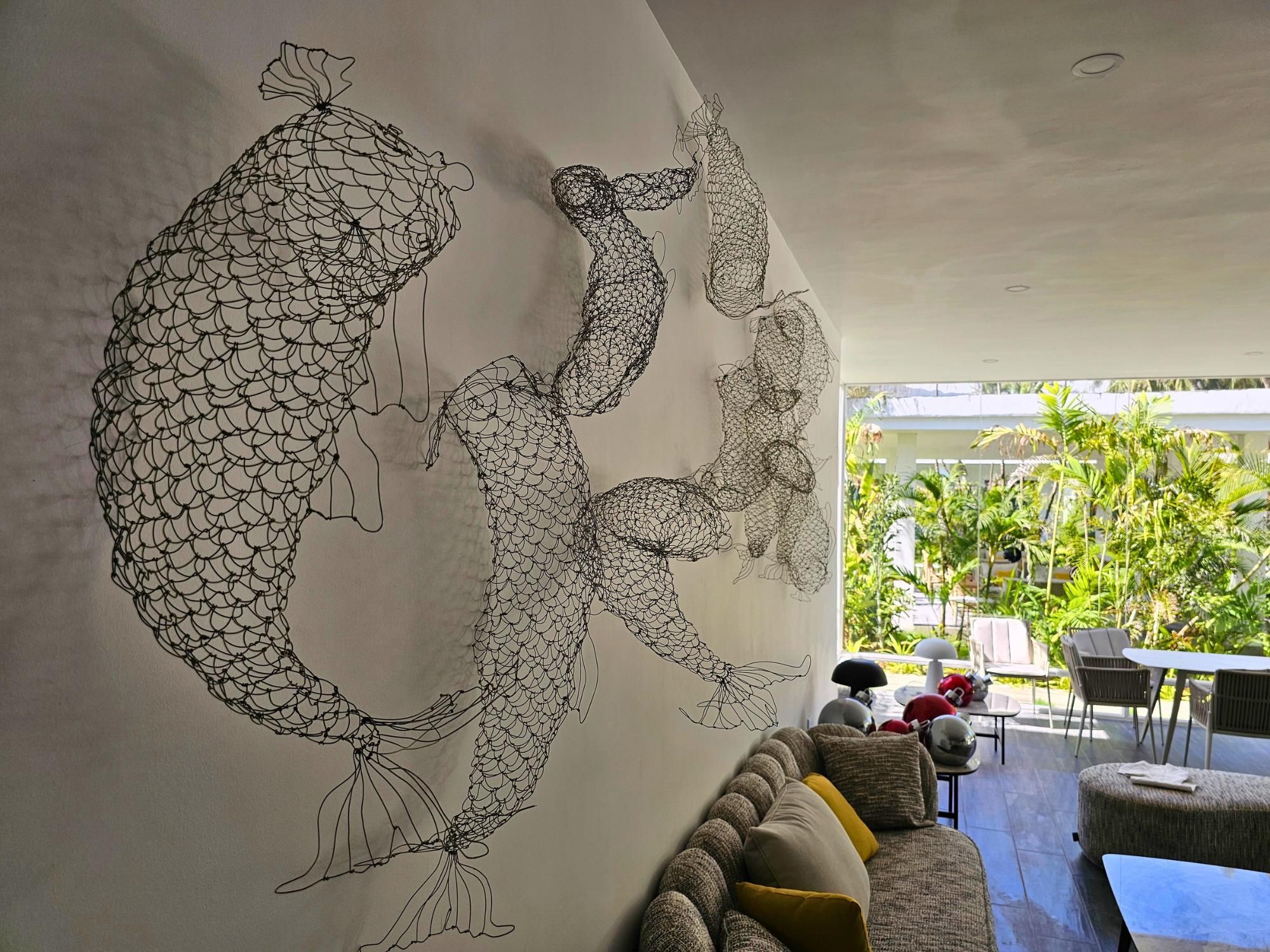 A modern interior with a large abstract wall art, a seating area with a sofa and chairs, and a view of greenery outside.