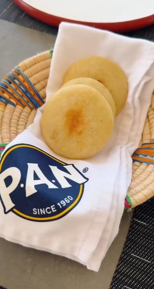 A woven basket with a white cloth napkin on top, containing three round, golden-brown items.