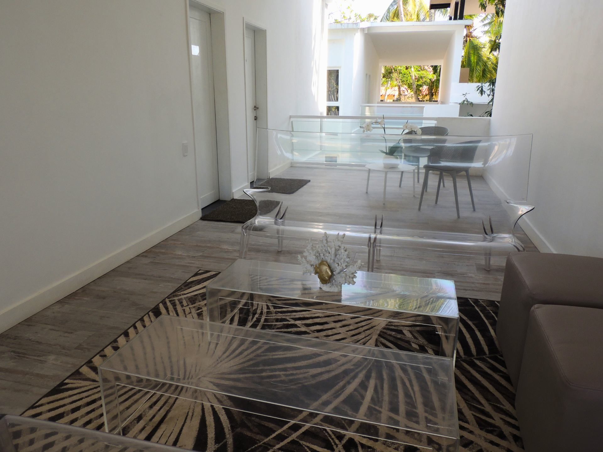 Un moderno salón con una mesa de centro de vidrio, un tapete estampado y vistas a un balcón con mobiliario exterior.