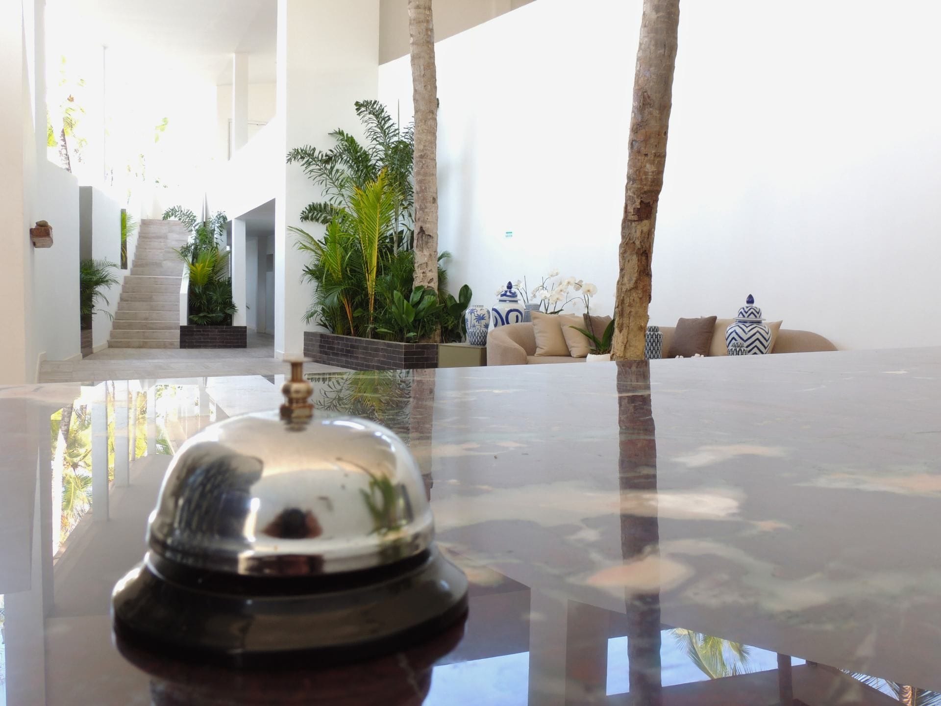 A hotel lobby with a reception desk, a staircase, and a seating area with plants and decorative items.