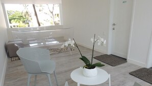 A modern room with a white chair, a small white table, and a potted orchid. There is a door and a window with a view of greenery outside. - Hotel Miragua Playa El Agua (Paraguachí)