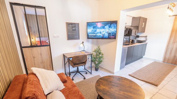 Una sala de estar moderna con un sofá, una mesa de centro, un televisor y una cocina con armarios y un microondas.