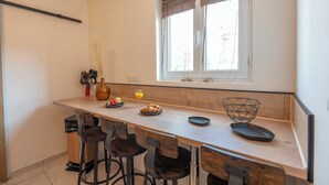Una cocina con mostrador de madera, taburetes de bar, una ventana con persianas y un lavamanos pequeño.