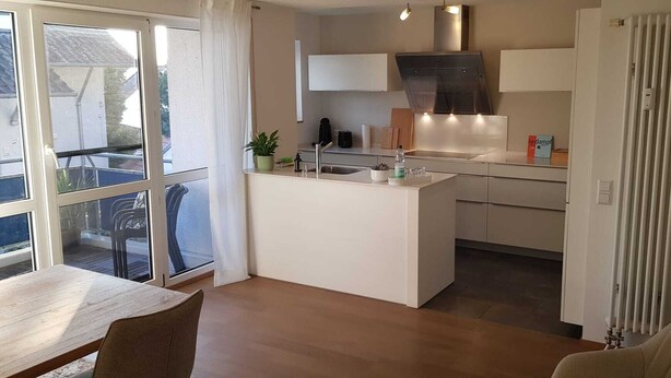 Une cuisine moderne dotée d’un îlot central, d’un coin repas avec une table et des chaises, et offrant une vue sur l’extérieur grâce à une grande fenêtre.