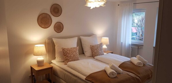 A bedroom with a bed, two bedside tables, a window, and three wall decorations.