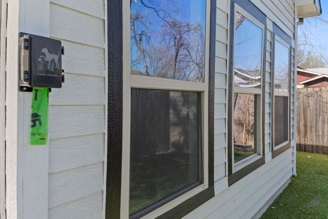 A house with large windows, a dog house, and a green sign on the side.