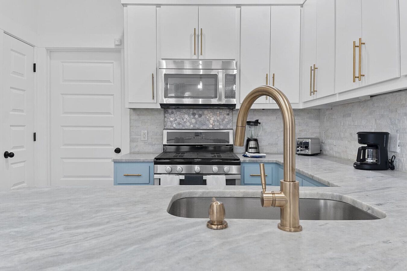 A modern kitchen with white cabinets, a stainless steel stove, a double sink with a gold faucet, and a coffee maker.