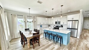 Una cocina moderna con armarios blancos, una isla central con taburetes y una zona de comedor con una mesa y sillas de madera.