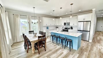 Una cocina moderna con armarios blancos, una isla central con taburetes y una zona de comedor con una mesa y sillas de madera.