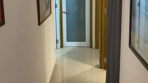 Un pasillo con una puerta que da a una habitación, un cuadro en la pared y una cortina a la derecha.