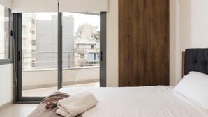 Ein Schlafzimmer mit einer großen Glasschiebetür, die auf einen Balkon führt, einem Bett mit weißer Bettwäsche und einer Holzverkleidung an der Wand.