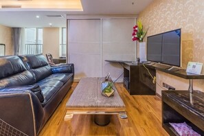 A living room with a black leather sofa, a wooden coffee table, a flat-screen TV, and a small plant.