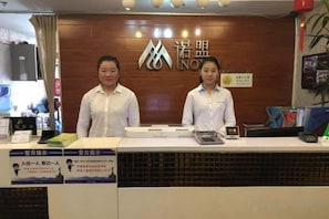 A reception desk with two staff members, a wooden backdrop with a logo, and a counter with various items including a calculator. - Hemu International Apartment (Guangzhou)