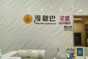 A hotel reception area with a marble wall, a reception desk, and a sign for 'Mianxiba Apartment.' - Hemu International Apartment (Guangzhou)