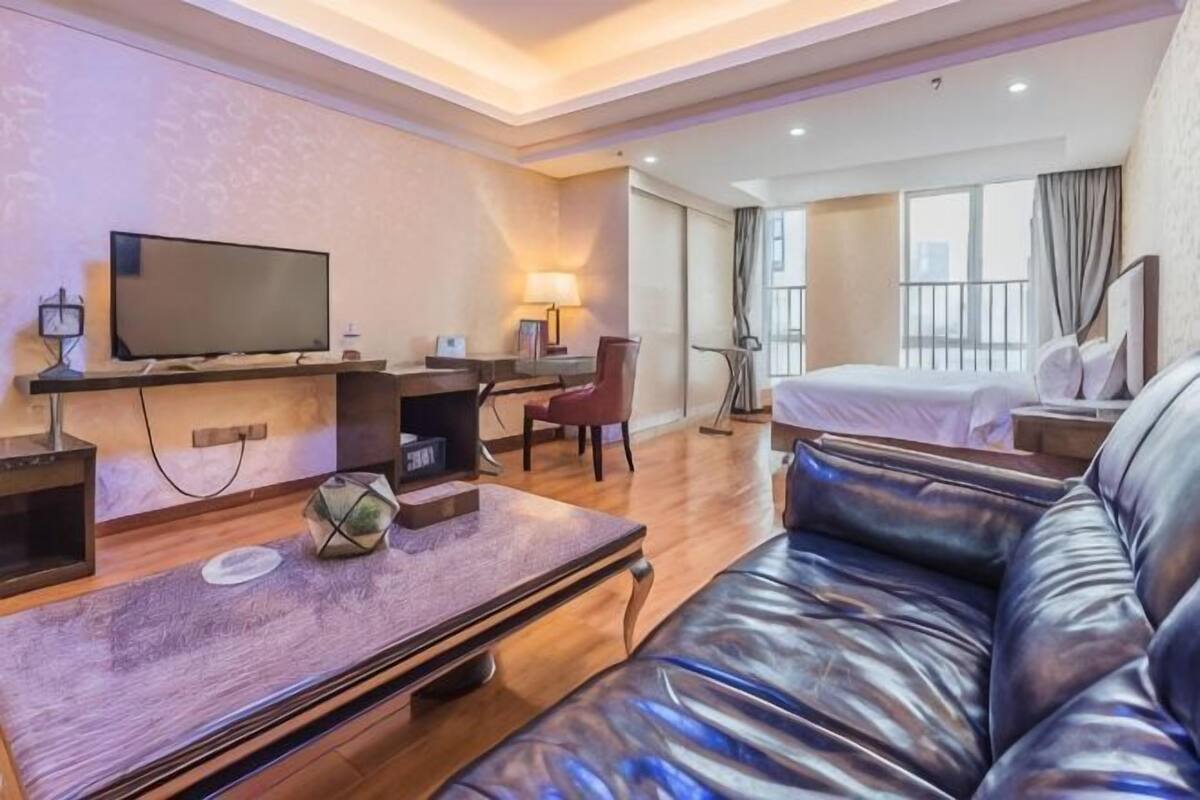 Une chambre d’hôtel équipée d’une télévision à écran plat, d’un bureau avec une chaise, d’un canapé en cuir, d’un lit et d’une grande fenêtre.