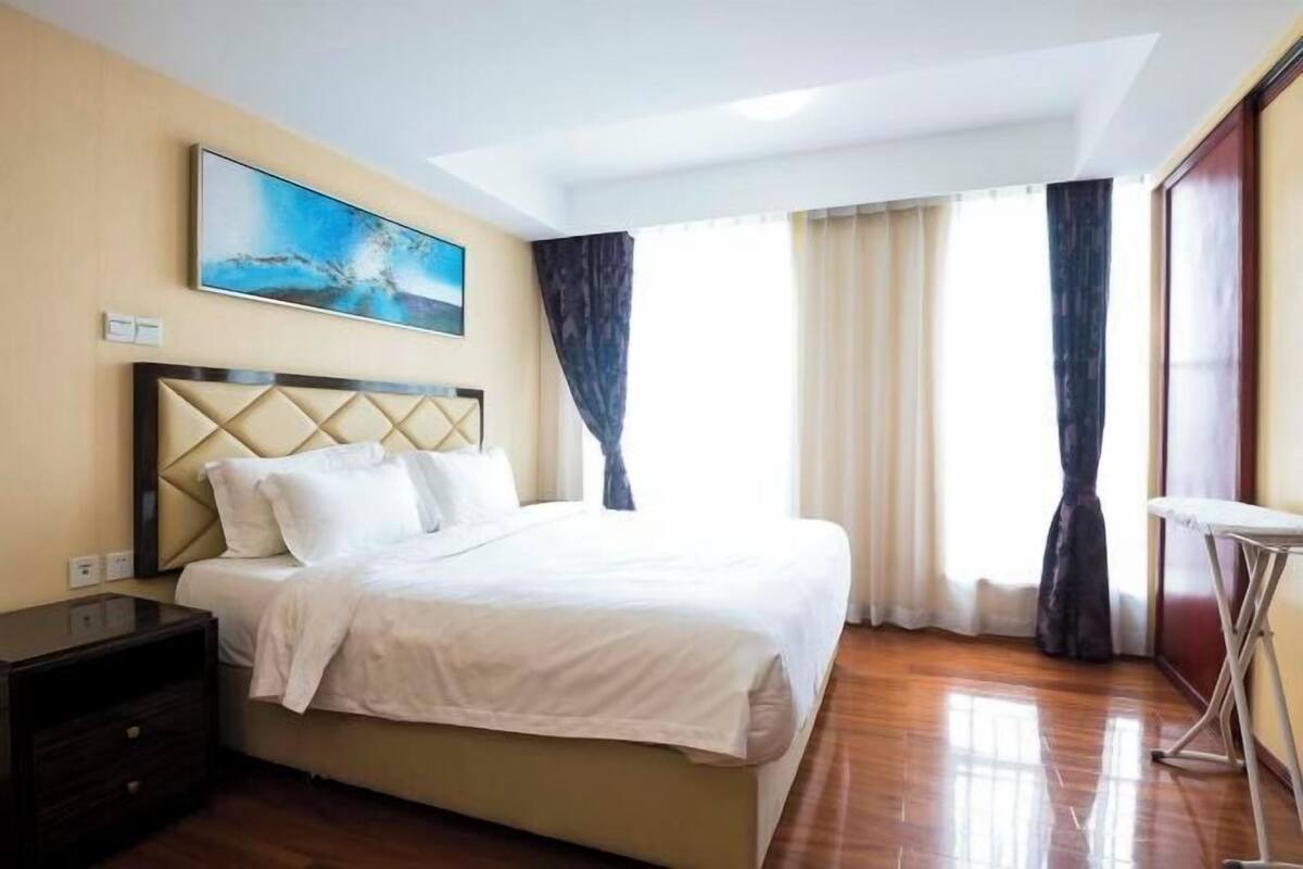 Une chambre d’hôtel avec un lit, une table de chevet, un tableau au mur et une fenêtre avec des rideaux.