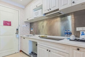 A modern kitchen with white cabinets, a stainless steel backsplash, a microwave, and a coffee maker.