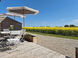 A wooden deck with outdoor furniture, a planter with flowers, and a field of yellow flowers in the background. - Kvarnviks Gård (Trelleborg)