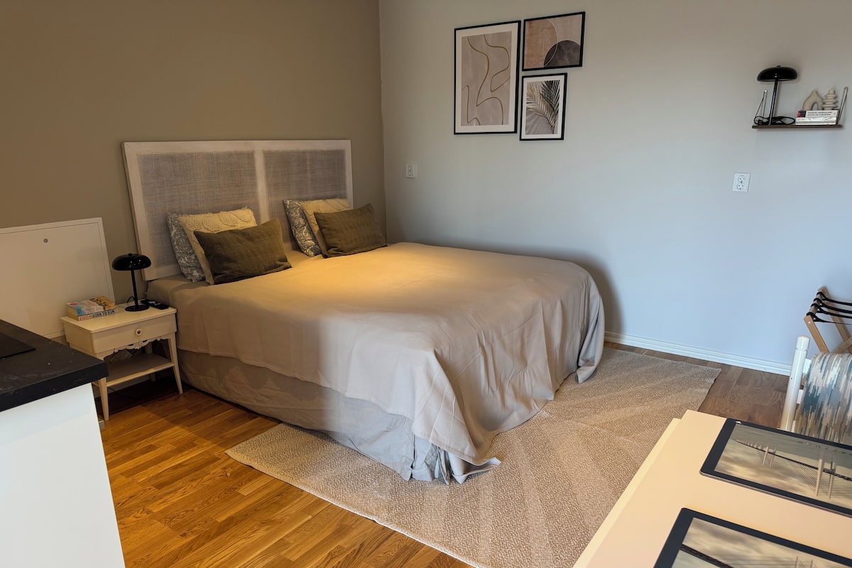 A bedroom with a bed, nightstand, bedside lamp, and a wall with framed pictures.