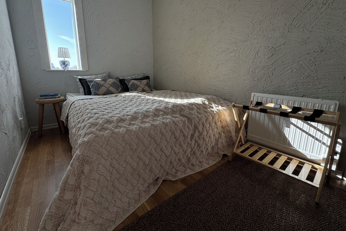 A bedroom with a bed, a window, a radiator, and a small table.