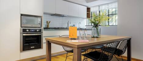 A modern kitchen with white cabinets, a wooden dining table, and black wire chairs.