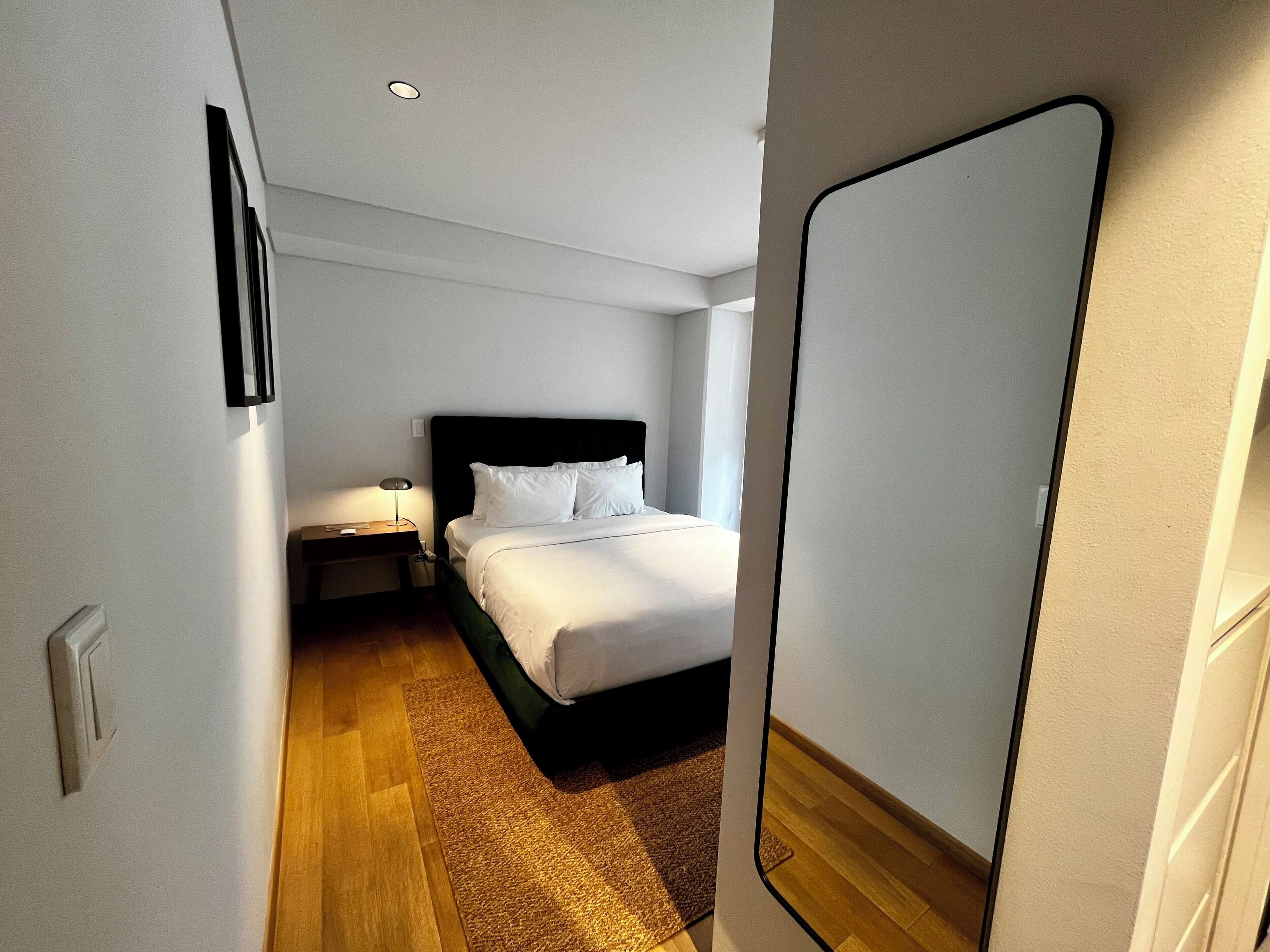 Una habitació d'hotel amb llit, taulella de nit, làmpada i mirall.
