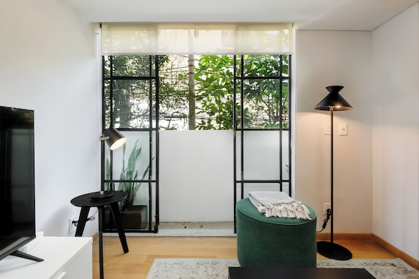 A modern living room with a large window, a floor lamp, a green ottoman, and a television. - Oaxaca by Wynwood House (Mexico City)
