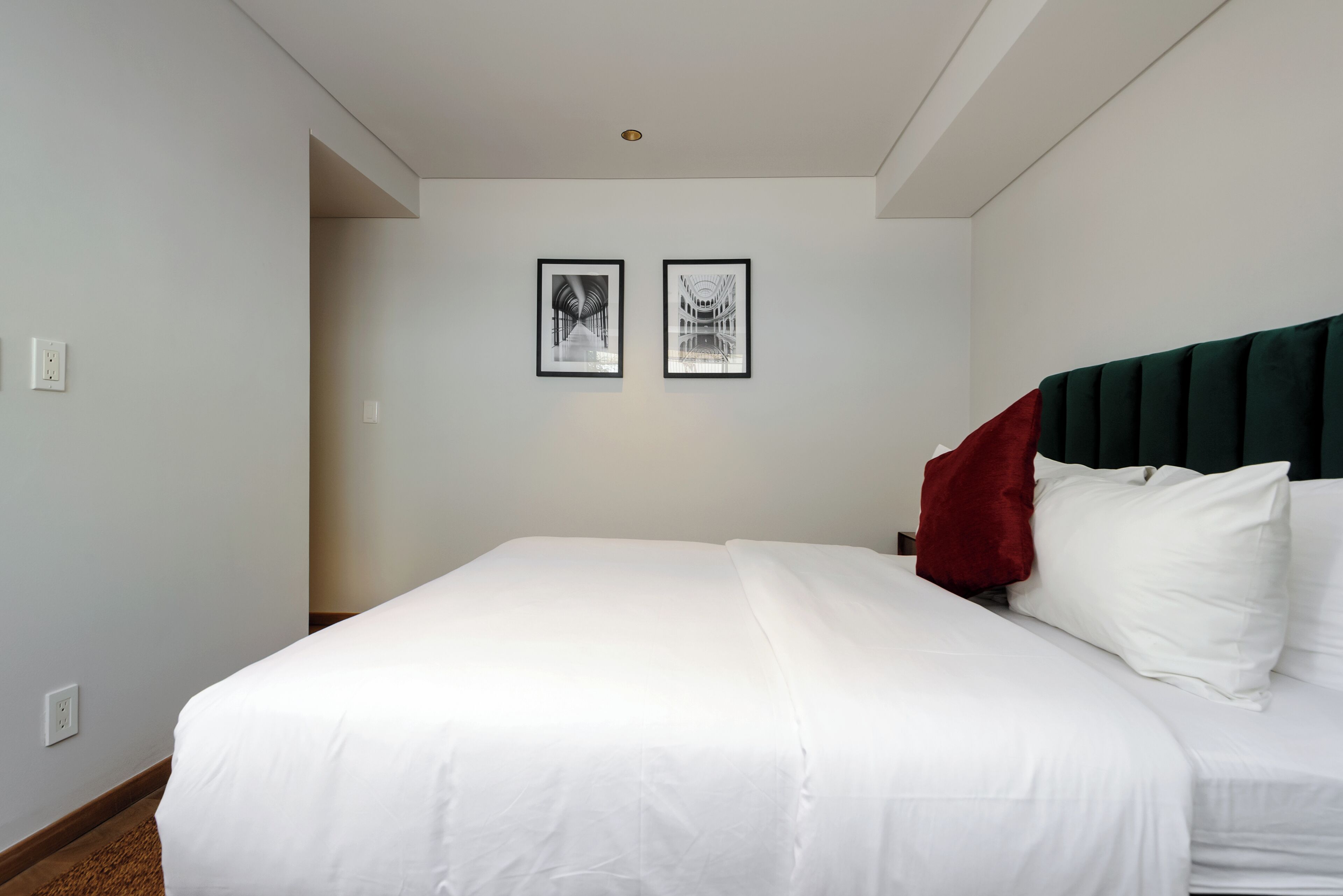 Een hotelkamer met een groot bed, een rode sierkussen en twee ingelijste foto's aan de muur.