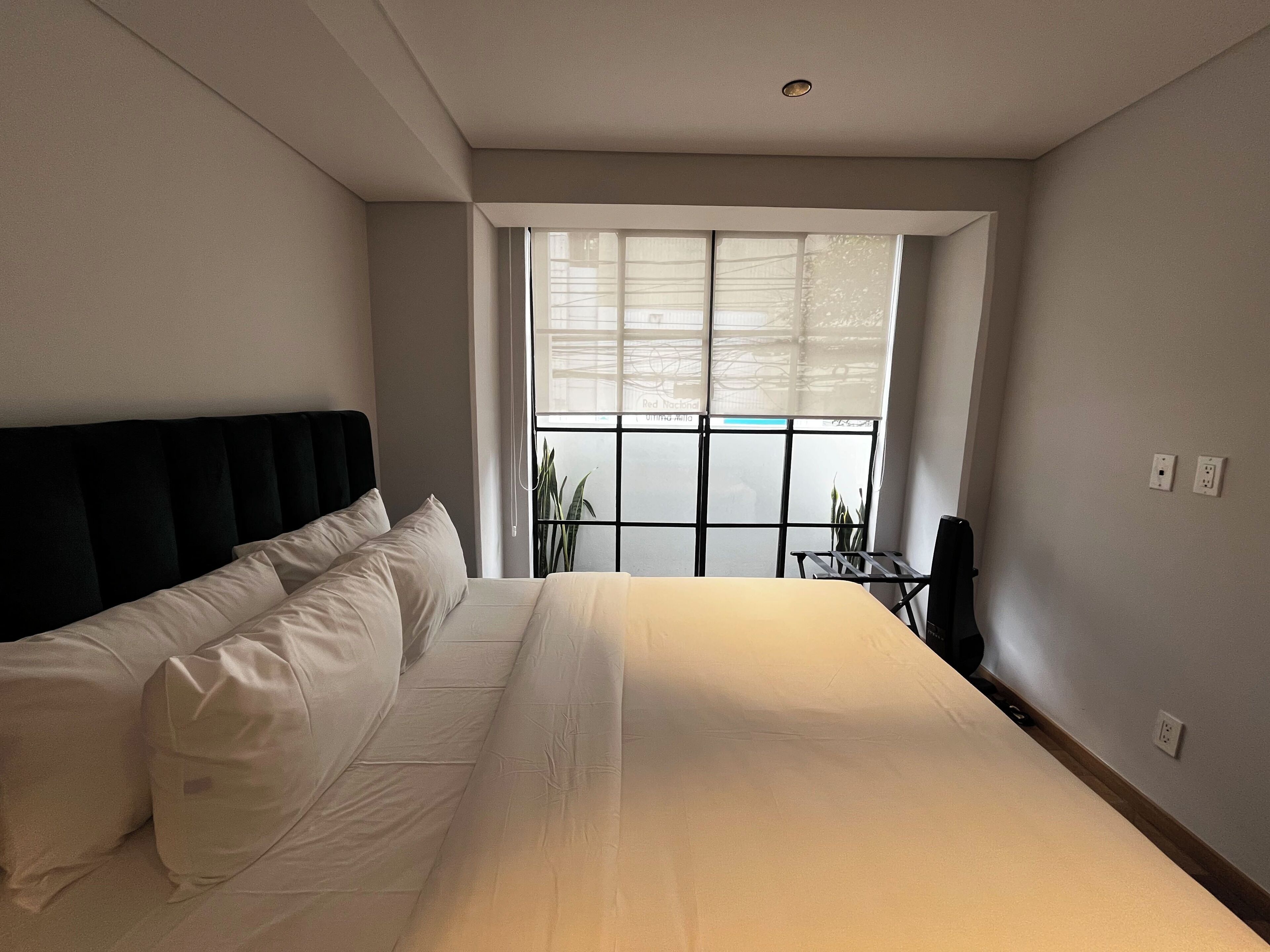 Ein modernes Hotelzimmer mit einem großen Bett, einem Schreibtisch und einem Fenster mit Jalousien.