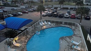 A swimming pool with lounge chairs, a blue canopy, and a view of a parking lot and buildings in the background. - Forget your worries in this spacious and serene space. (Gulf Shores)