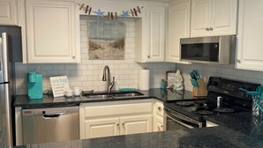 A kitchen with white cabinets, a stainless steel refrigerator, a microwave, and a stove. - Forget your worries in this spacious and serene space. (Gulf Shores)