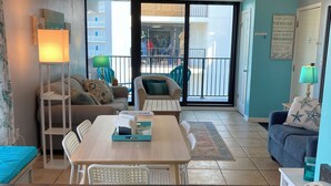A modern living room with a dining area, a sofa, a coffee table, and a balcony with a view of the city. - Forget your worries in this spacious and serene space. (Gulf Shores)