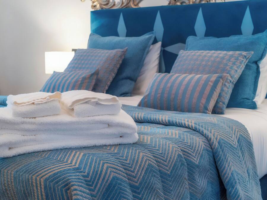 Una cama bien hecha con ropa de cama azul y blanca, una pila de toallas blancas y almohadas a juego.