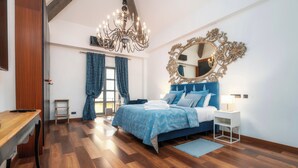 A bedroom with a wooden floor, a bed with blue bedding, a chandelier, a large mirror, and a small bedside table. - Oakmoon House (Faro)