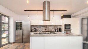 A modern kitchen with a central island, stainless steel appliances, and pendant lighting. - Oakmoon House (Faro)