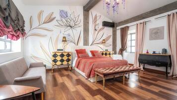 Een moderne slaapkamer met houten vloer, een bed met rood-wit gebedspread, een grijze bank, een houten bankje, een zwart piano, en een muur met bloem- en bladmotieven.