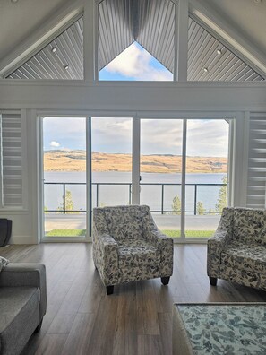 A spacious room with a large window overlooking a lake and hills. There are two patterned armchairs and a sofa. - House on Nicola Lake (Thompson-Nicola M (Beautiful *)