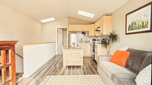 Eine moderne Küche mit Holzausstattung, ein Essbereich mit Tisch und Stühlen sowie eine Wohnbereich mit Sofa und Pflanze.