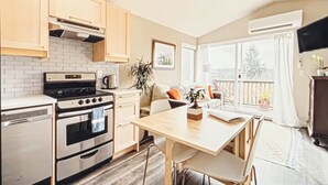 Eine moderne Küche mit Einbauofen, Geschirrspüler und Holzschränken. Ein Essbereich mit Tisch und Stühlen sowie ein Balkon mit Blick auf Bäume.